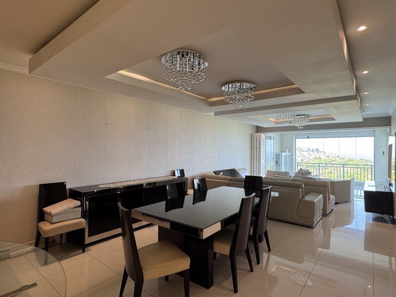 Spacious open-plan living and dining area featuring high-gloss floor tiles, recessed ceilings with crystal chandeliers, and large sliding doors leading to a balcony.