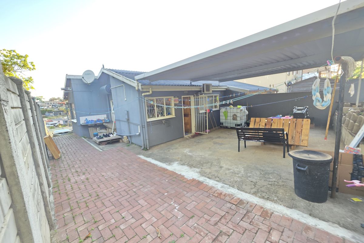 Rear exterior view of the townhouse featuring a paved driveway, a covered carport area, and perimeter security walling.