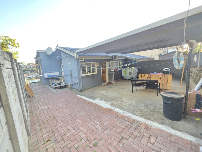 Rear exterior view of the townhouse featuring a paved driveway, a covered carport area, and perimeter security walling.