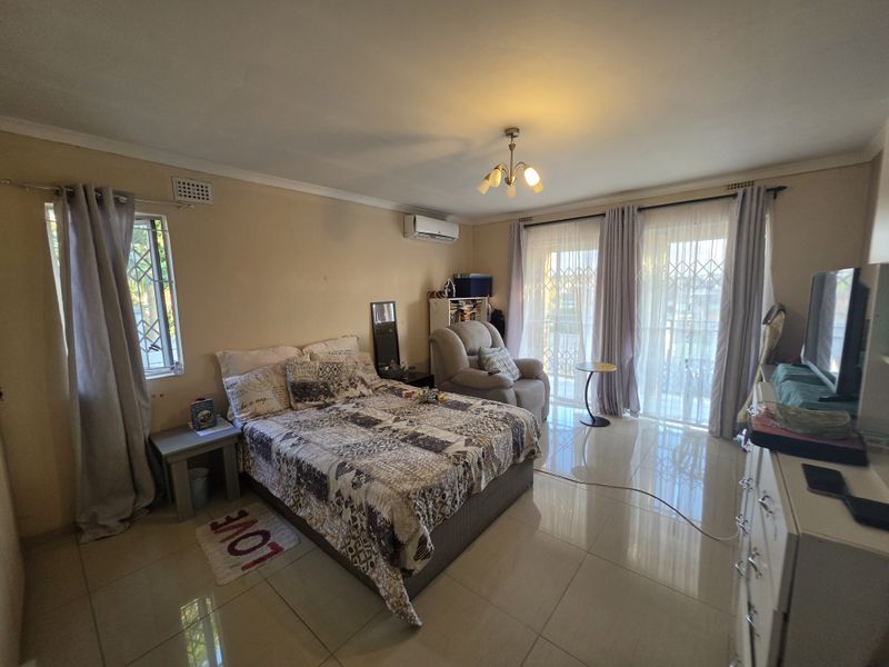 Spacious bedroom featuring tiled flooring, a split-system air conditioner, and direct access to a balcony through sliding glass doors with security gates.