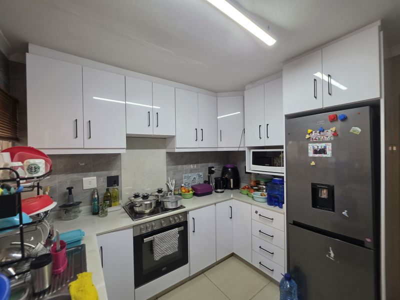 A functional kitchen featuring white gloss cabinetry, a built-in oven, hob, and stone-look backsplash, providing a clean and practical workspace.