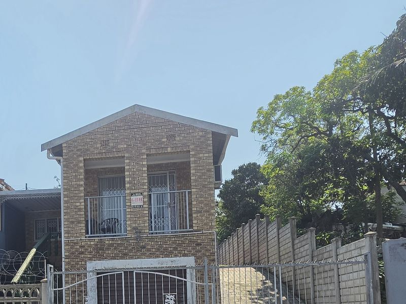 Front elevation of a face brick townhouse featuring a metal security gate, concrete driveway, and an upper-level balcony with security bars.