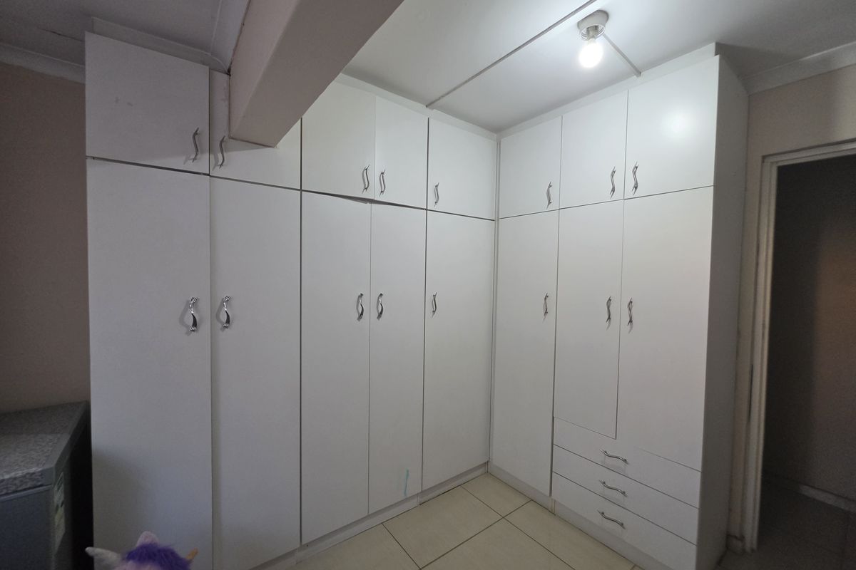 A bedroom featuring extensive white built-in cupboards with ample storage space and neutral tiled flooring.
