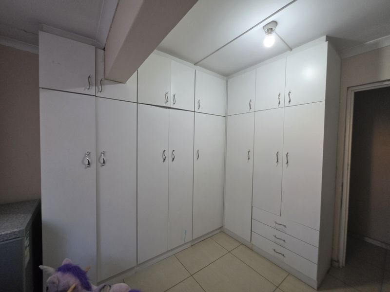 A bedroom featuring extensive white built-in cupboards with ample storage space and neutral tiled flooring.
