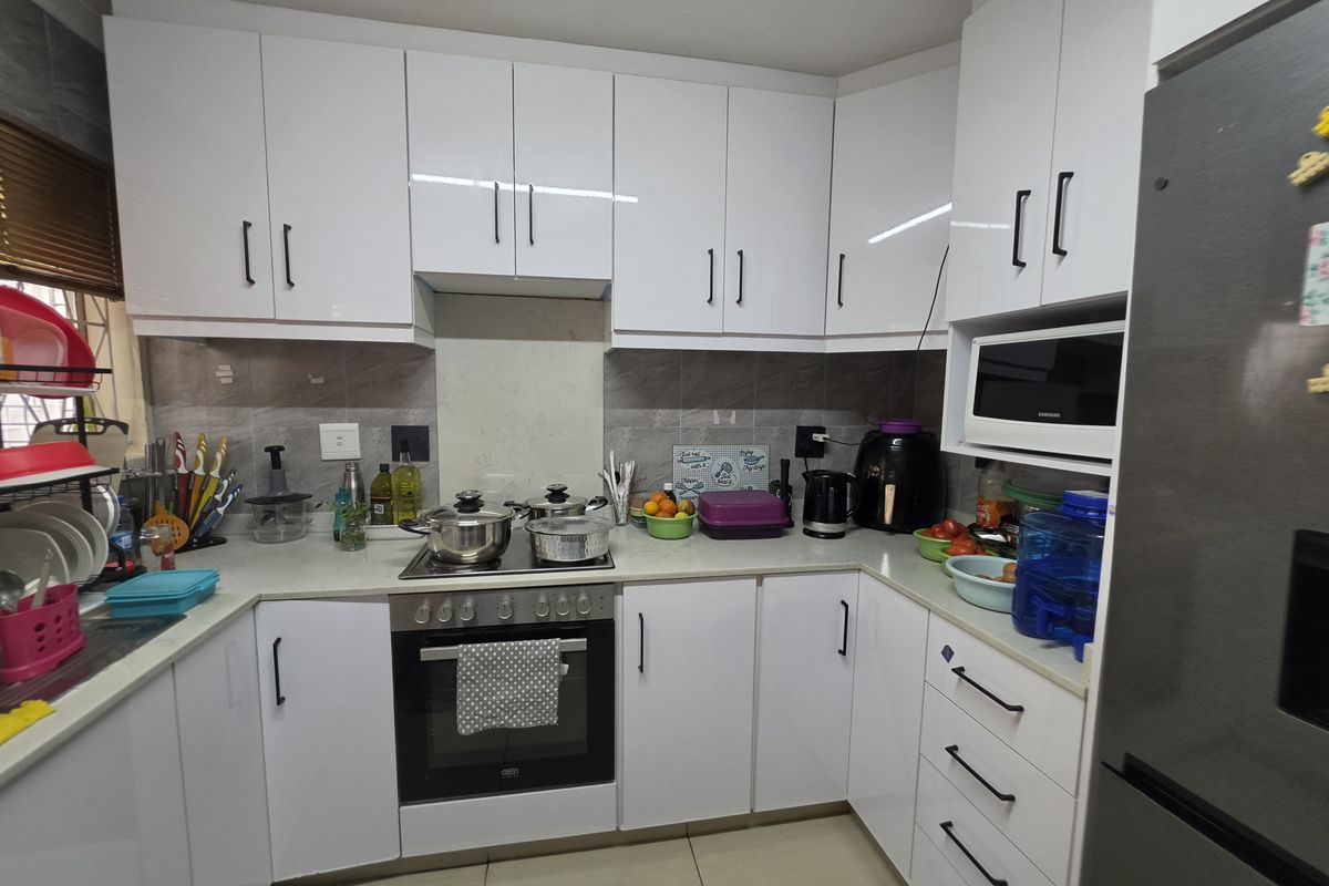 A modern, well-maintained kitchen featuring white cabinetry, stone countertops, a built-in oven, electric hob, and integrated microwave with a tiled backsplash.