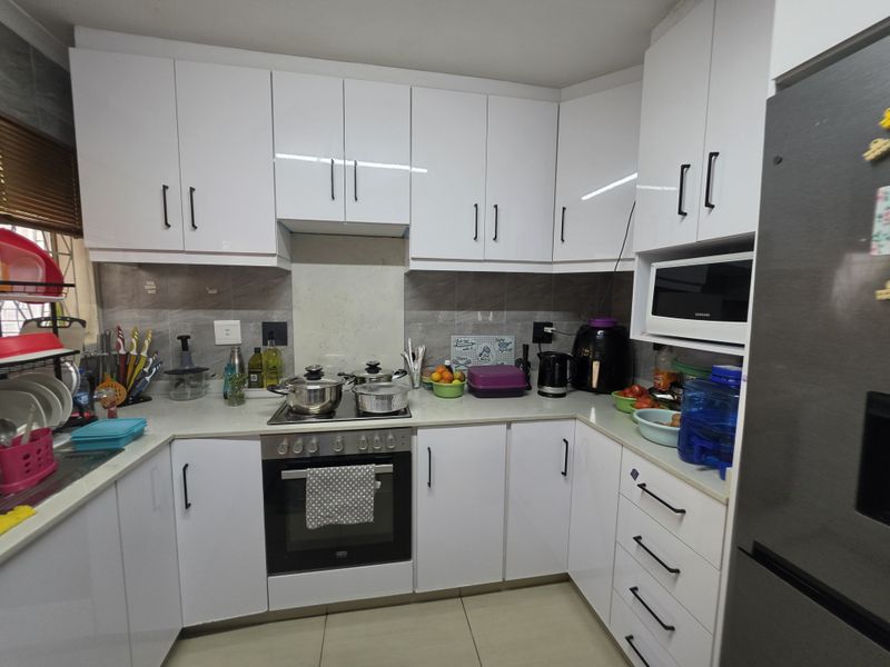A modern, well-maintained kitchen featuring white cabinetry, stone countertops, a built-in oven, electric hob, and integrated microwave with a tiled backsplash.