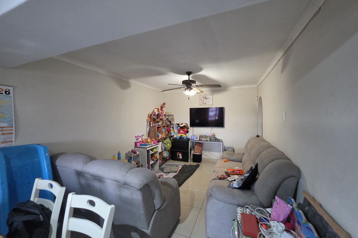 A functional living room featuring tiled flooring, coved cornicing, and a central ceiling fan, providing a comfortable space for daily relaxation.