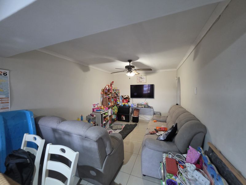 A functional living room featuring tiled flooring, coved cornicing, and a central ceiling fan, providing a comfortable space for daily relaxation.