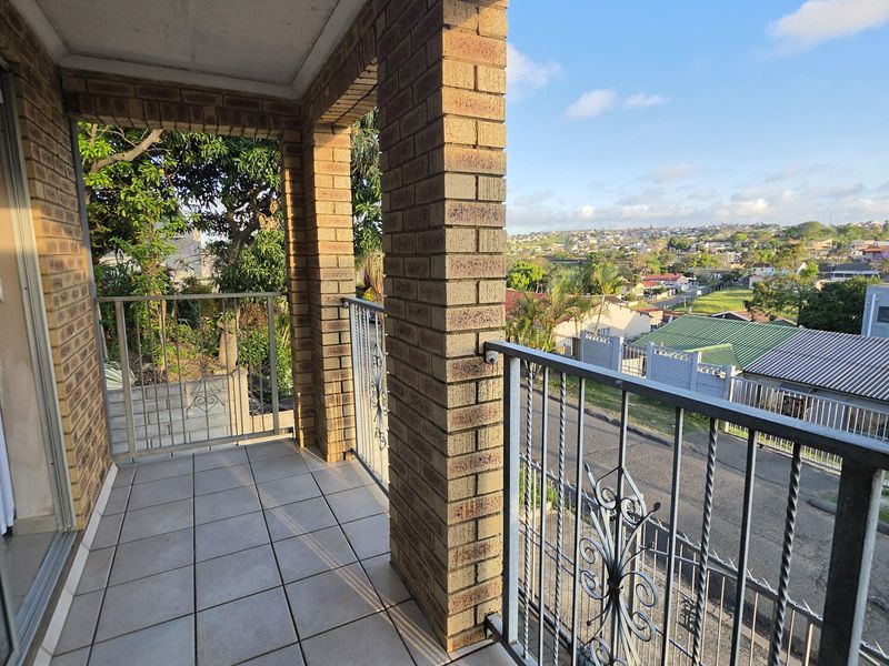 A covered balcony featuring brick pillars, tiled flooring, and a metal balustrade, offering elevated views of the surrounding neighborhood.