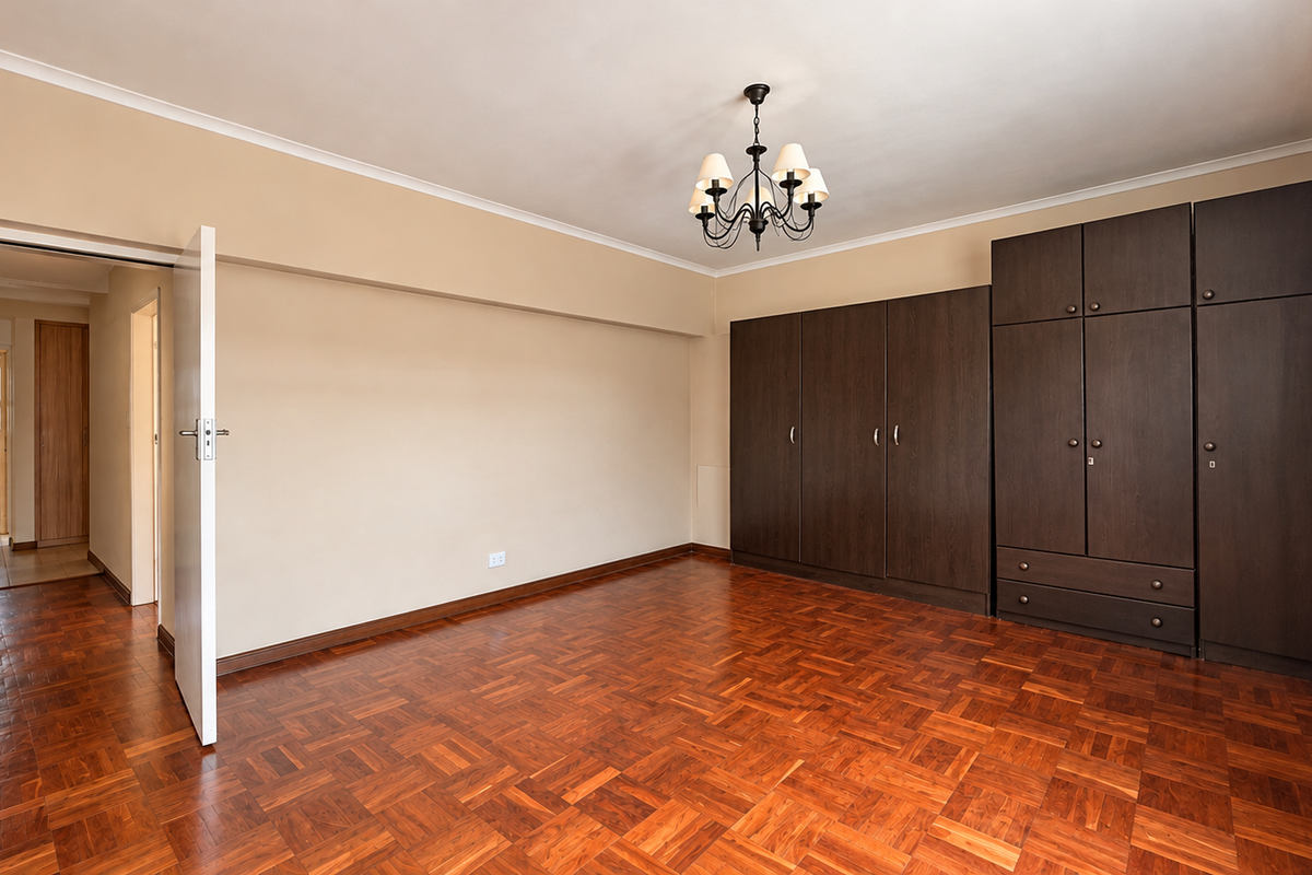 Spacious bedroom featuring warm parquet flooring, extensive dark wood built-in cupboards, and a classic chandelier, offering a clean and well-maintained living space.