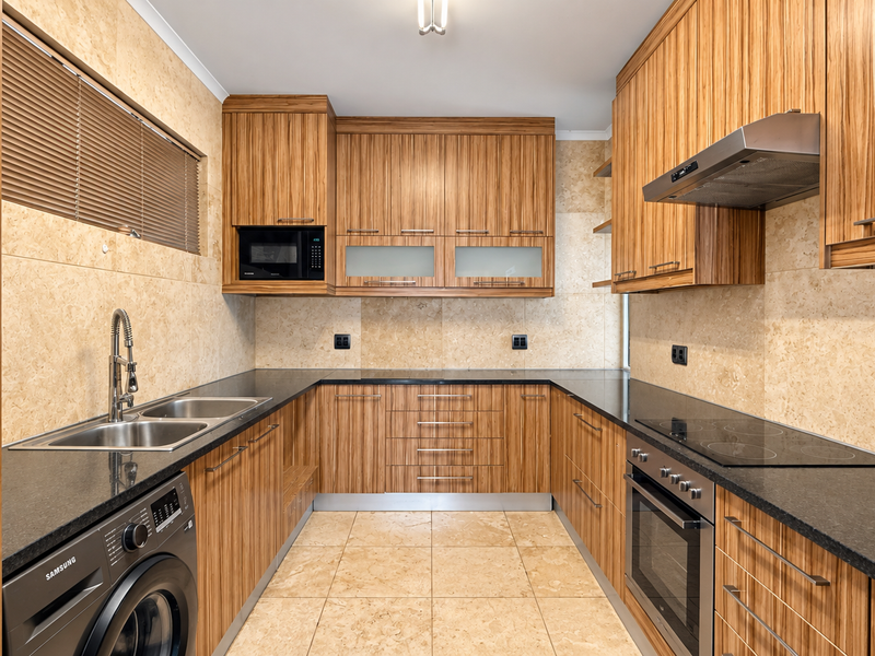 A well-maintained U-shaped kitchen featuring wood-grain cabinetry, granite countertops, integrated appliances, and neutral tiled finishes throughout.