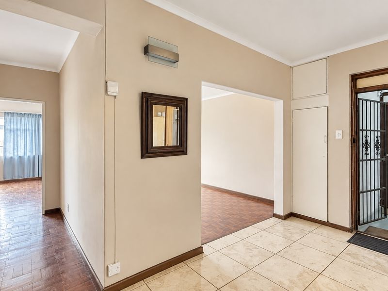 Entrance foyer featuring tiled flooring, a built-in storage cupboard, and a security gate, leading into a spacious interior with parquet flooring.