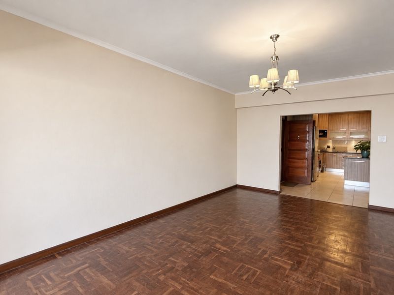 Spacious open-plan living area featuring classic parquet flooring, a central chandelier, and a seamless transition into the adjacent kitchen space.