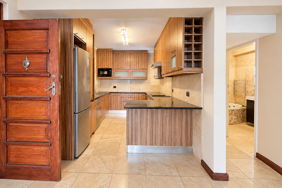 A well-maintained kitchen featuring wood-finish cabinetry, granite countertops, and tiled flooring, with an open-plan layout and adjacent bathroom access.