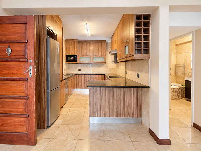 A well-maintained kitchen featuring wood-finish cabinetry, granite countertops, and tiled flooring, with an open-plan layout and adjacent bathroom access.