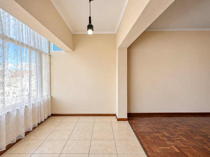 A bright, empty living area featuring a combination of ceramic tile and parquet wood flooring, large windows, and a modern pendant light fixture.