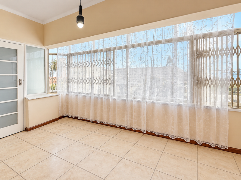 A bright and spacious enclosed balcony featuring tiled flooring, large windows with security gates, and a modern frosted glass door.