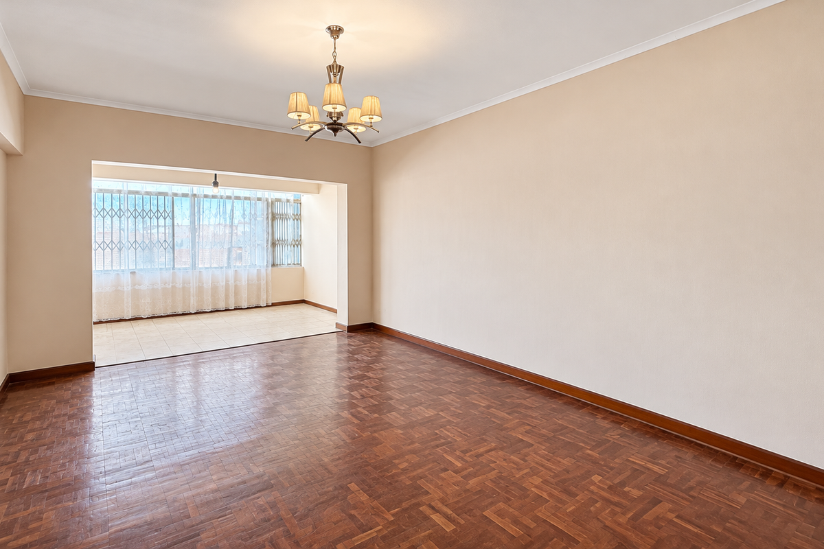 Spacious, empty living area featuring classic parquet flooring, a central chandelier, and an adjoining enclosed balcony with security gates.