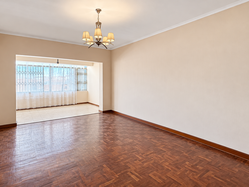 Spacious, empty living area featuring classic parquet flooring, a central chandelier, and an adjoining enclosed balcony with security gates.