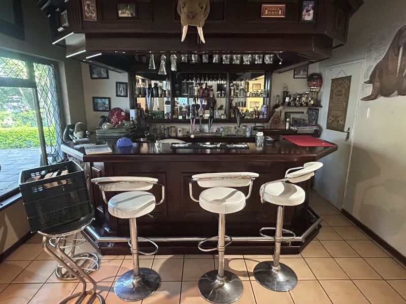 A dedicated home bar area featuring a substantial built-in wooden counter, mirrored back bar with integrated glass storage, and classic tiled flooring.
