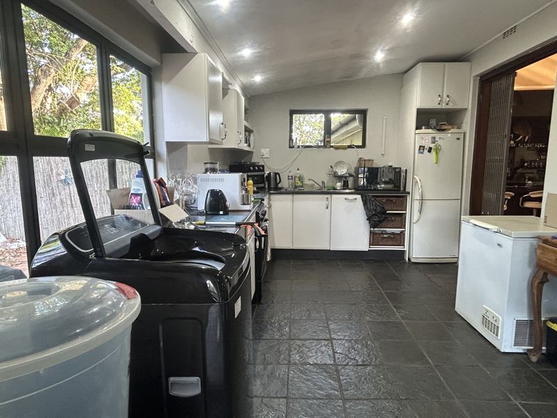 A functional scullery or utility area featuring built-in cabinetry, a sink, and tiled flooring, providing ample space for laundry and kitchen preparation tasks.
