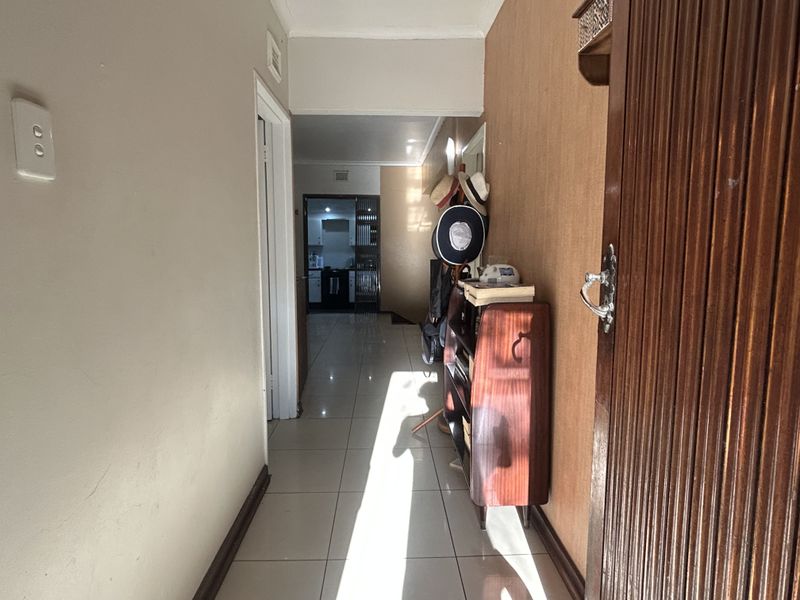 A functional hallway featuring tiled flooring and a wooden entrance door, providing a clear transition through the home towards the kitchen area.