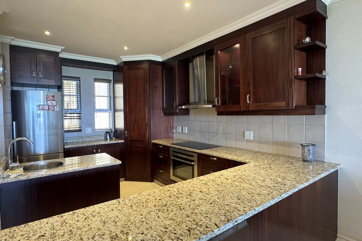 A well-appointed kitchen featuring dark wood cabinetry, granite countertops, a built-in oven, electric hob, and a stainless steel extractor fan.