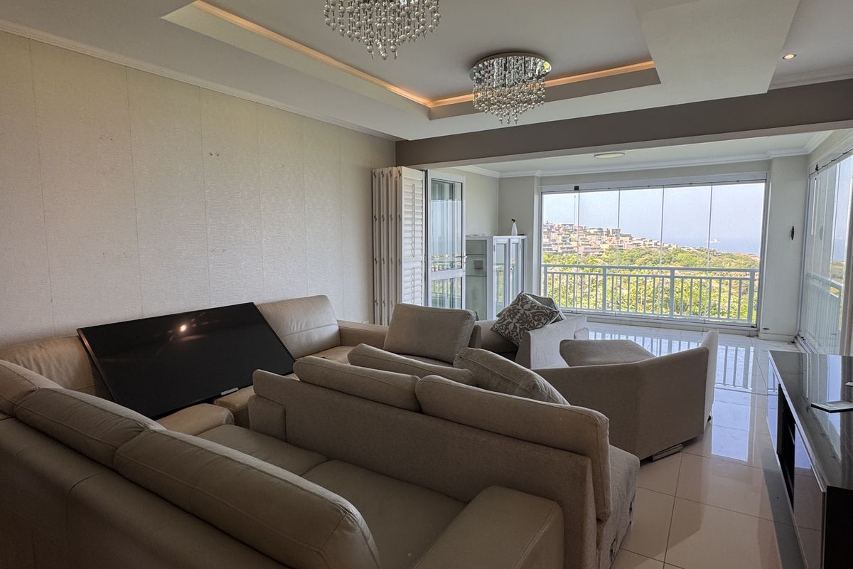Spacious living room featuring recessed ceiling with cove lighting, tiled floors, and large glass sliding doors opening onto a balcony with scenic views.