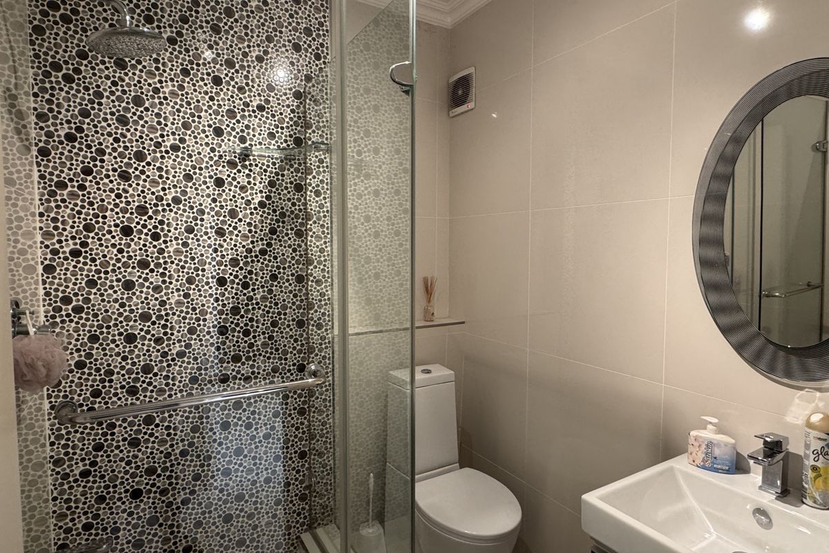 Modern bathroom featuring a walk-in shower with decorative mosaic tiling, a glass screen, a wall-mounted toilet, and a sleek vanity basin.