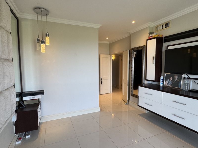 A well-maintained bedroom featuring tiled flooring, recessed lighting, and built-in cabinetry, leading into a hallway with additional internal doors.
