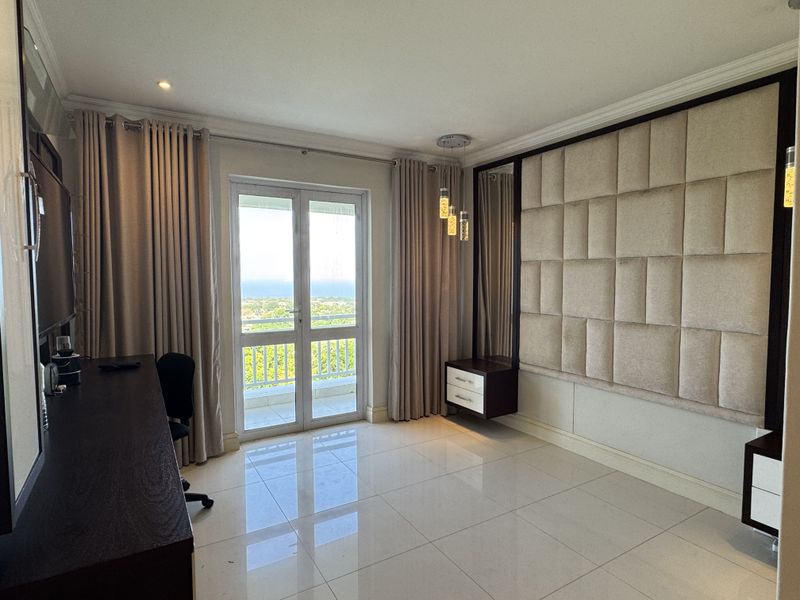 A well-maintained bedroom featuring modern upholstered wall paneling, floating cabinetry, polished tile floors, and direct access to a private balcony with scenic views.