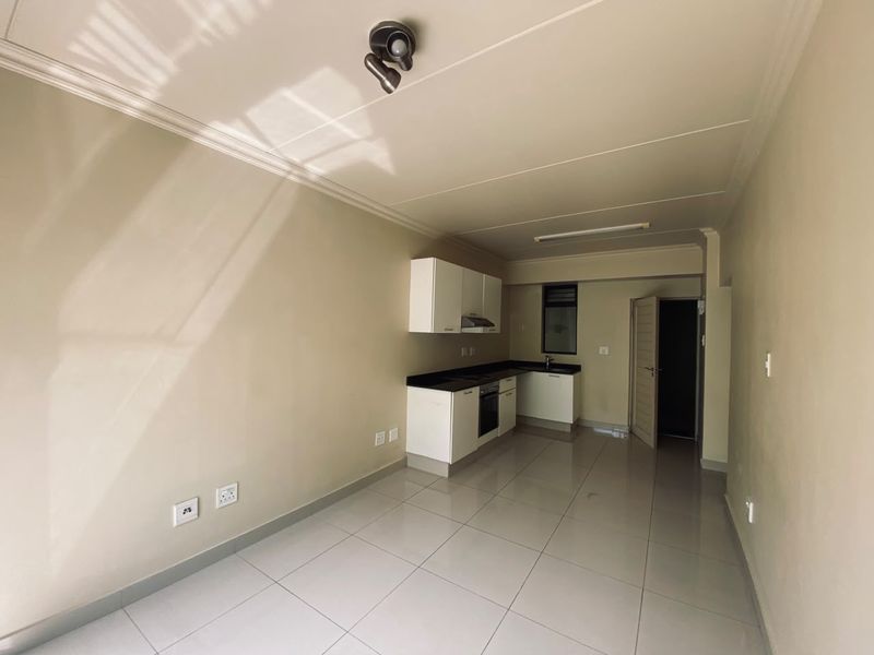 An open-plan living and kitchen area featuring neutral walls, tiled flooring, and a functional kitchen with built-in cabinetry and appliances.