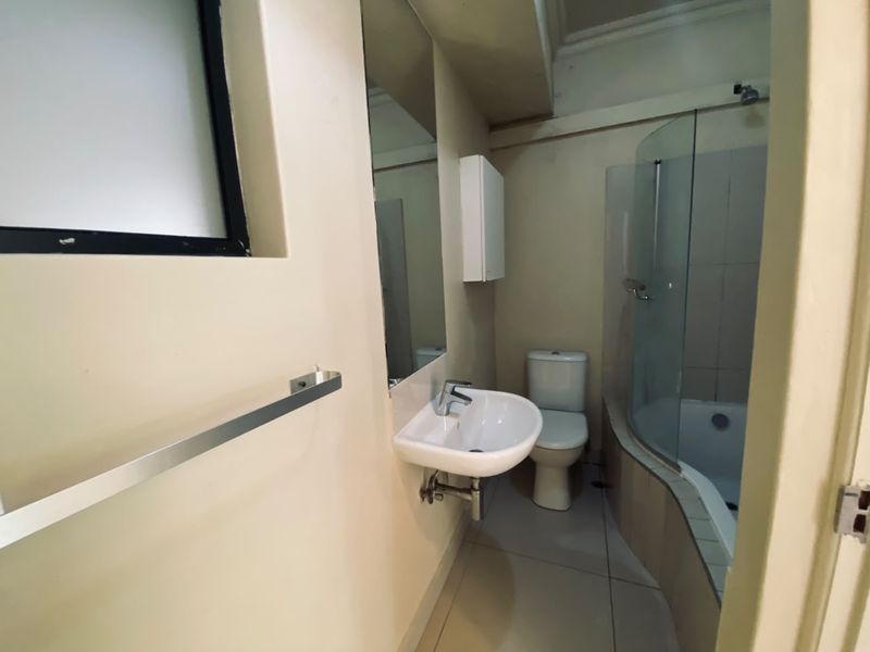 A functional bathroom featuring a wall-mounted basin, toilet, and a curved glass shower enclosure with tiled flooring.