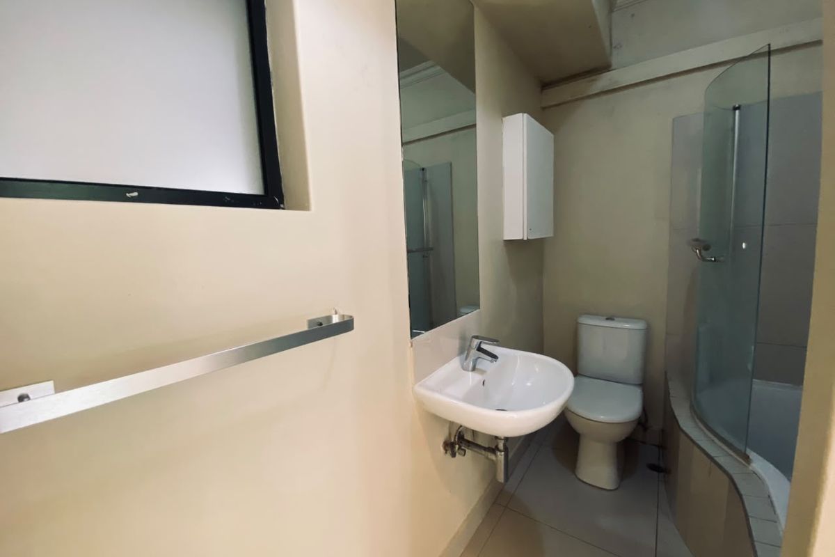 A functional bathroom featuring a wall-mounted basin, toilet, and a curved glass shower enclosure with tiled flooring.