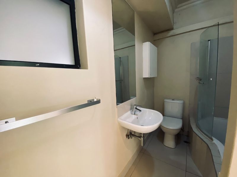 A functional bathroom featuring a wall-mounted basin, toilet, and a curved glass shower enclosure with tiled flooring.