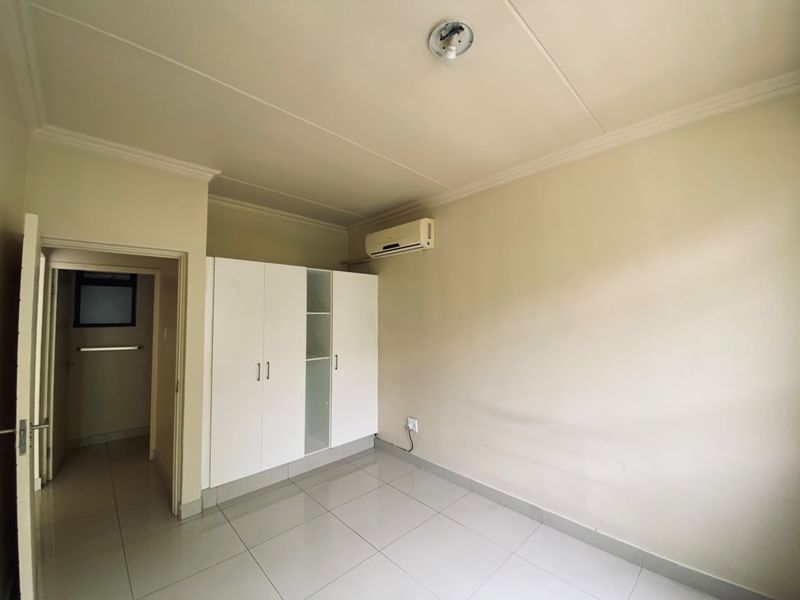A clean, empty bedroom featuring tiled flooring, built-in cupboards, and an air conditioning unit, ready for personalization.