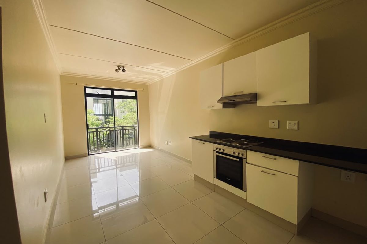 An open-plan living and kitchen area featuring tiled floors, modern white cabinetry, built-in oven and hob, and access to a private balcony.