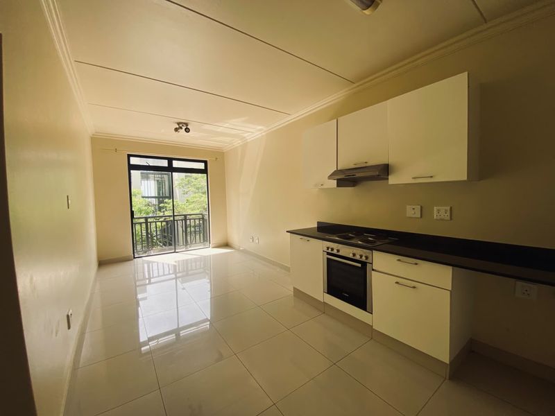 An open-plan living and kitchen area featuring tiled floors, modern white cabinetry, built-in oven and hob, and access to a private balcony.