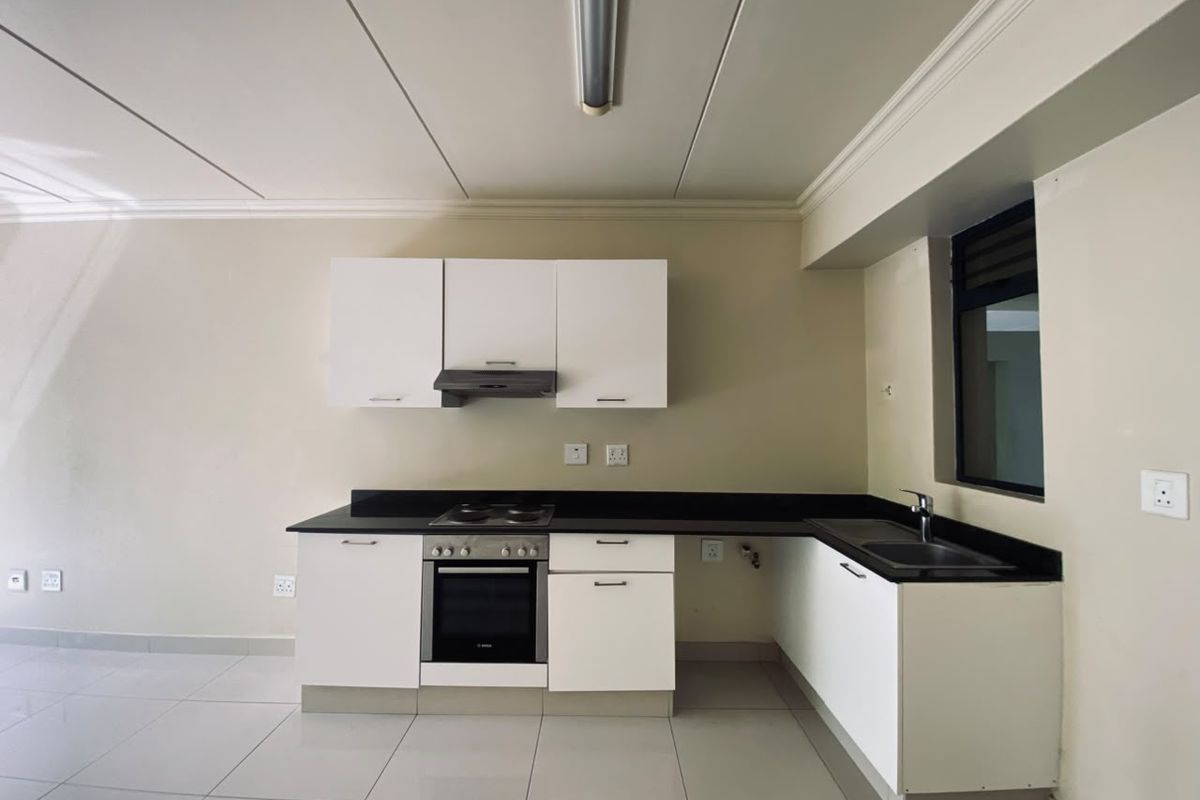 A clean, modern kitchen featuring white cabinetry, black granite countertops, integrated oven and hob, and neutral tiled flooring.