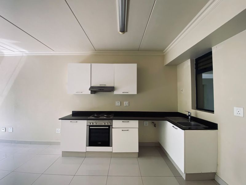 A clean, modern kitchen featuring white cabinetry, black granite countertops, integrated oven and hob, and neutral tiled flooring.
