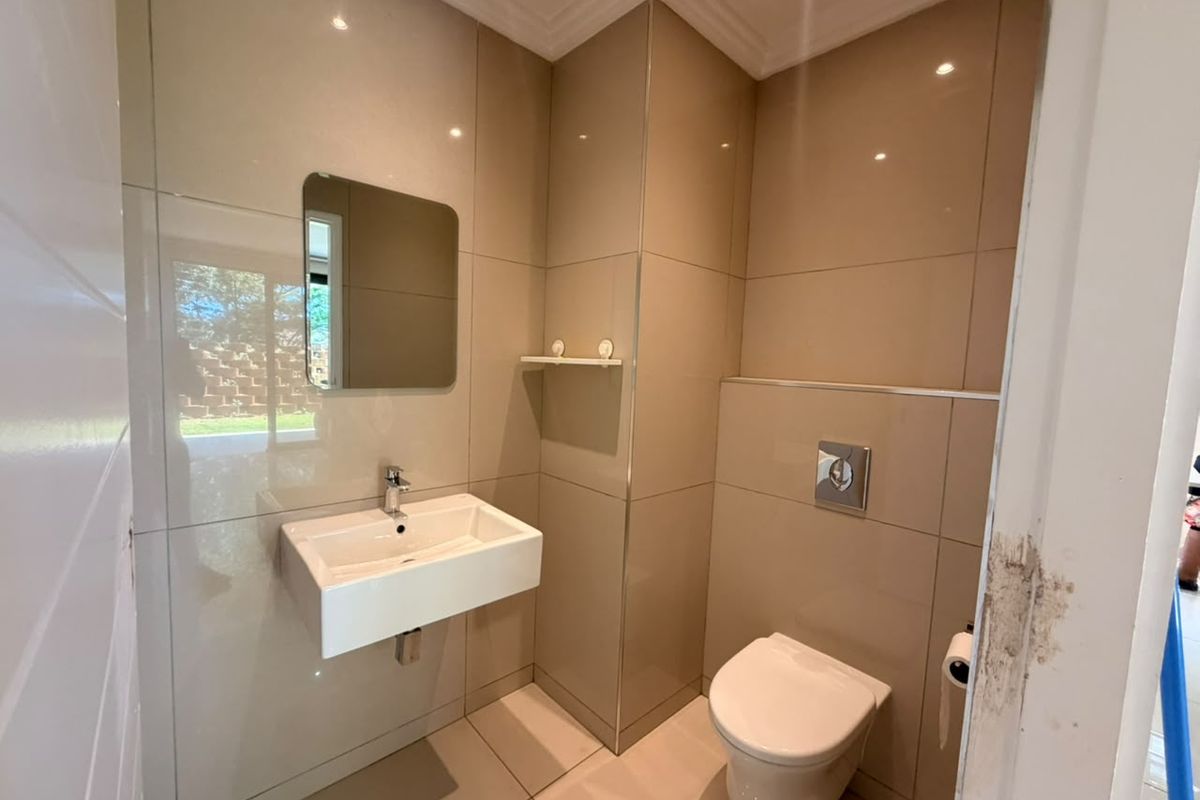 A modern guest bathroom featuring floor-to-ceiling ceramic tiling, a wall-mounted basin, and a concealed cistern toilet with chrome flush plate.