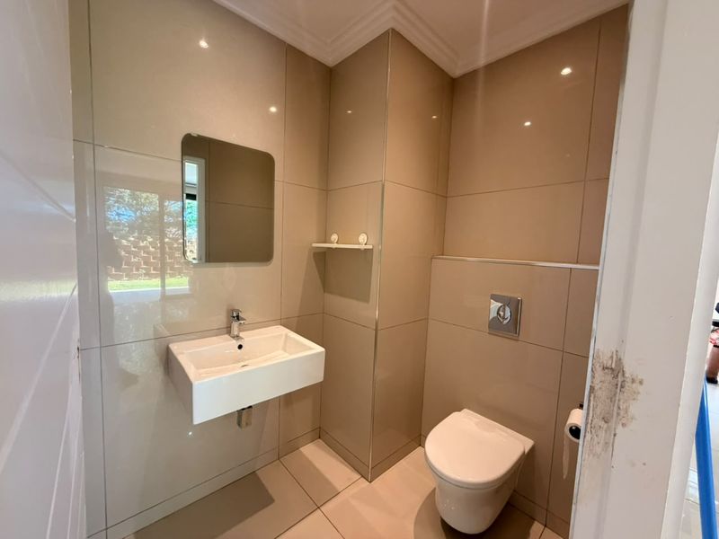 A modern guest bathroom featuring floor-to-ceiling ceramic tiling, a wall-mounted basin, and a concealed cistern toilet with chrome flush plate.