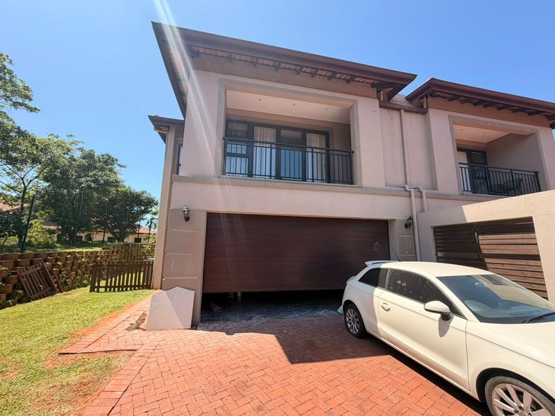 Front elevation of a double-storey townhouse featuring a double garage, upper-level balcony, and brick-paved driveway.