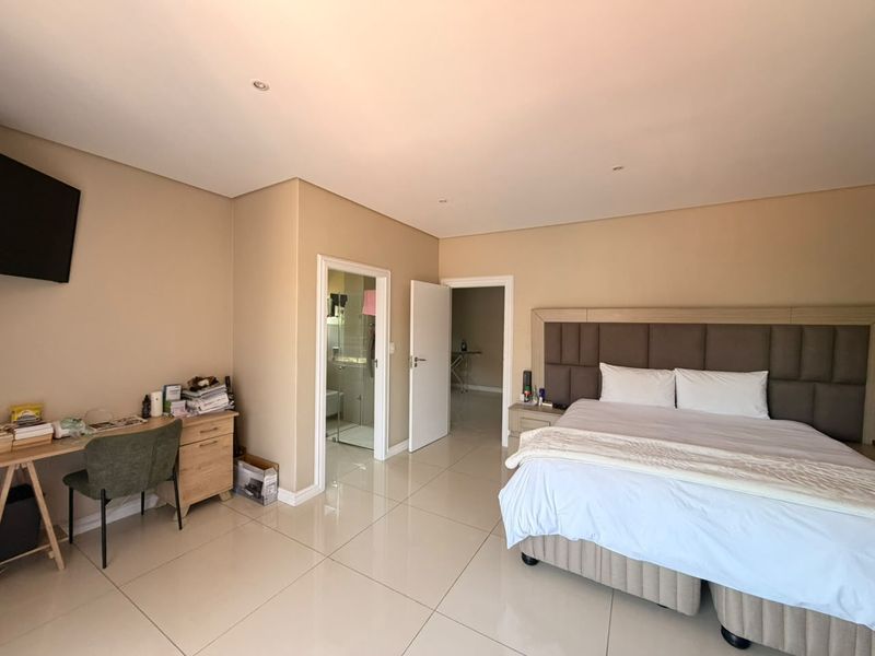 Spacious bedroom featuring tiled flooring, recessed lighting, and an integrated headboard, with direct access to an en-suite bathroom.