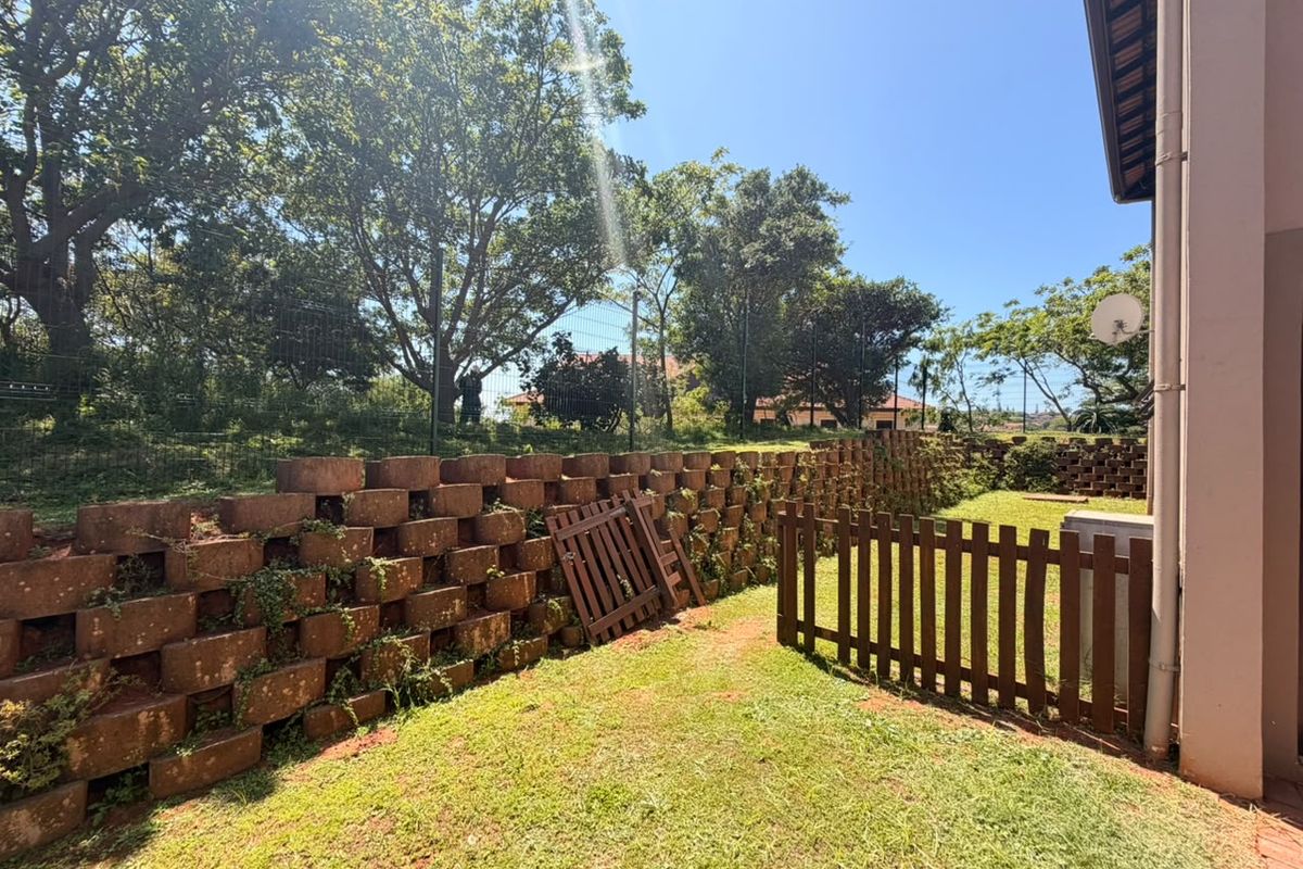 A private rear garden area featuring a tiered retaining wall, lawn space, and perimeter fencing.
