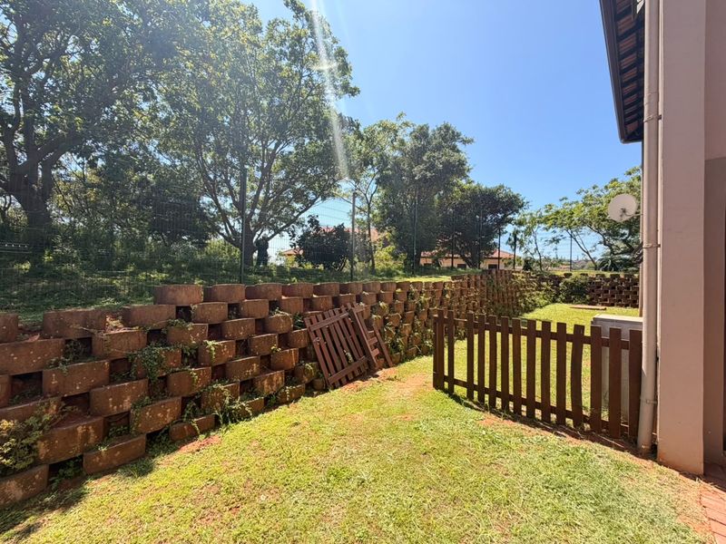 A private rear garden area featuring a tiered retaining wall, lawn space, and perimeter fencing.