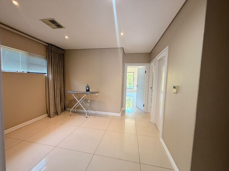 A bright and spacious bedroom featuring neutral wall tones, polished porcelain floor tiles, recessed downlighting, and ducted air conditioning.
