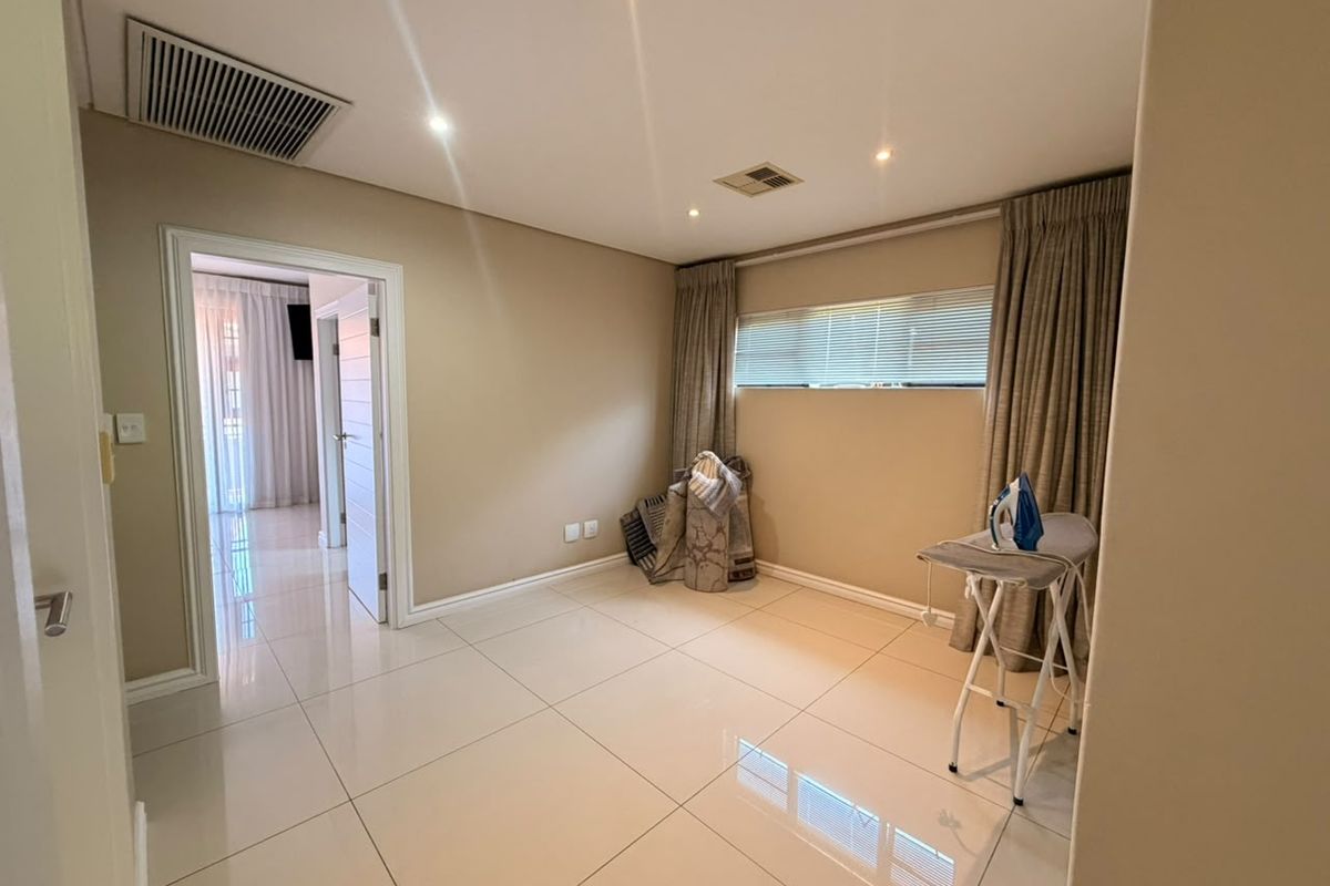 A bright and spacious bedroom featuring neutral wall tones, polished porcelain floor tiles, recessed downlighting, and ducted air conditioning.