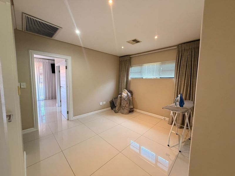 A bright and spacious bedroom featuring neutral wall tones, polished porcelain floor tiles, recessed downlighting, and ducted air conditioning.
