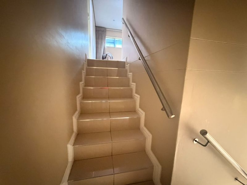 A functional staircase featuring tiled steps and a modern stainless steel handrail, providing access between levels in the townhouse.